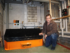 Ein Mann kniend neben einer Stückholzheizung des Produkttyps Novatronic XV von Schmid in einem Heizungsraum.